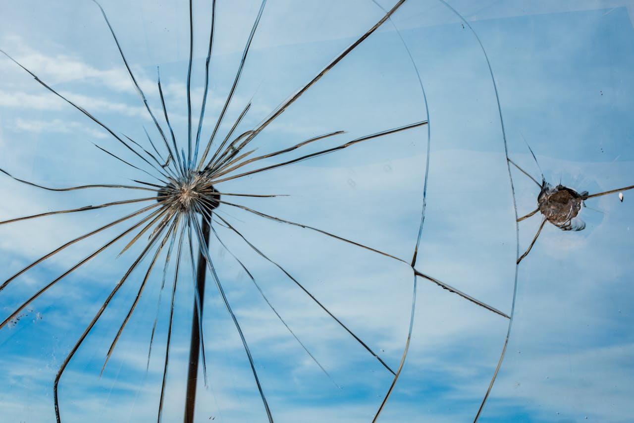 Dramatic shattered glass pattern against a clear blue sky, symbolizing fragility and resilience.
